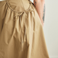 Close up of a person wearing a beige skirt with a white top, standing against a neutral background.