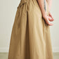 Person wearing beige skirt with a white top against a neutral background