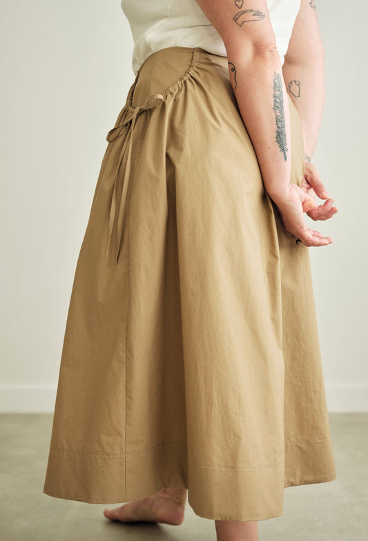 Person wearing beige skirt with a white top against a neutral background