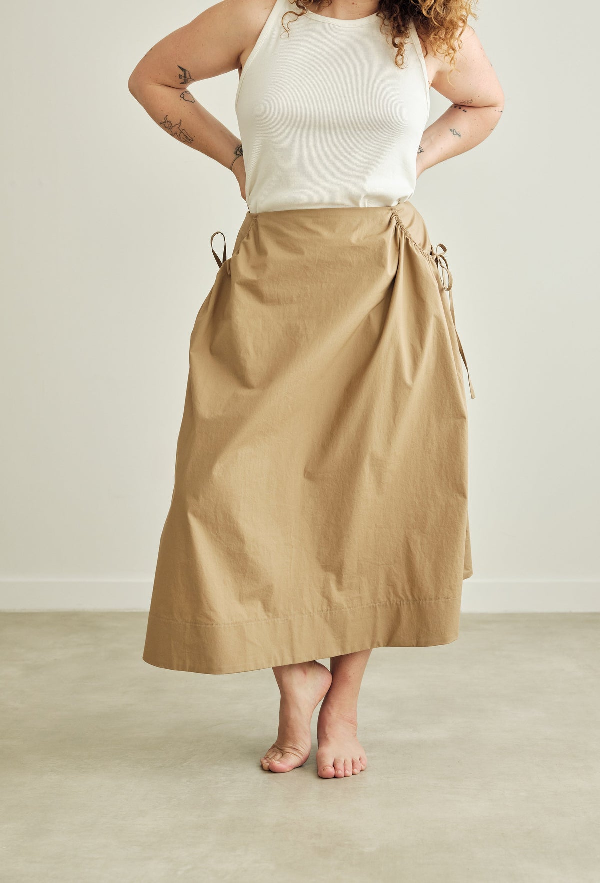 Person wearing a beige skirt and a white top on a plain background