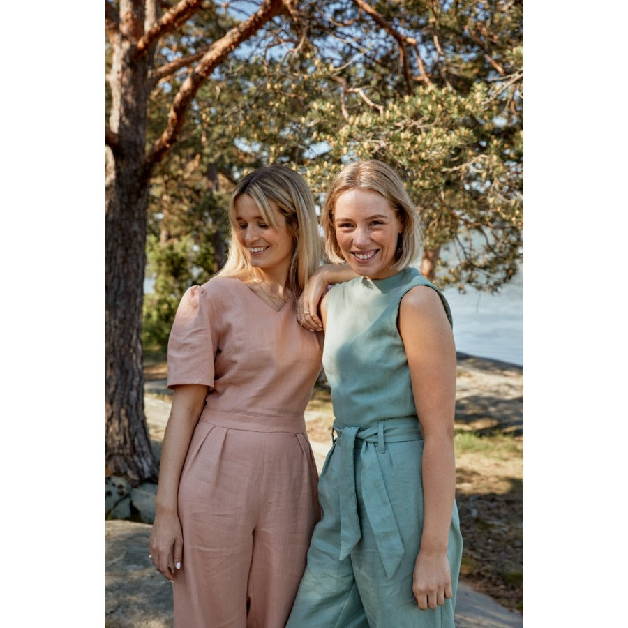 Two white women standing next to each other smiling wearing pastel coloured jumpsuits in the sunshine