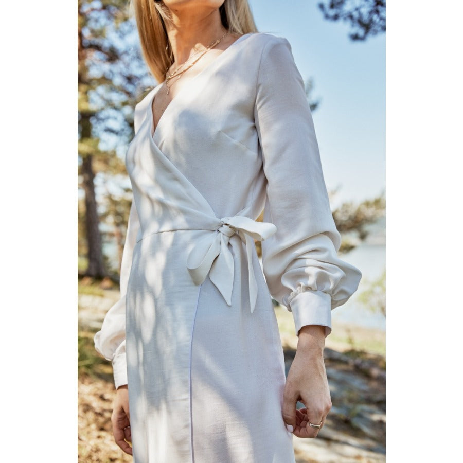 Close up of a white woman wearing a cream coloured wrap dress tied at the waist in a bow