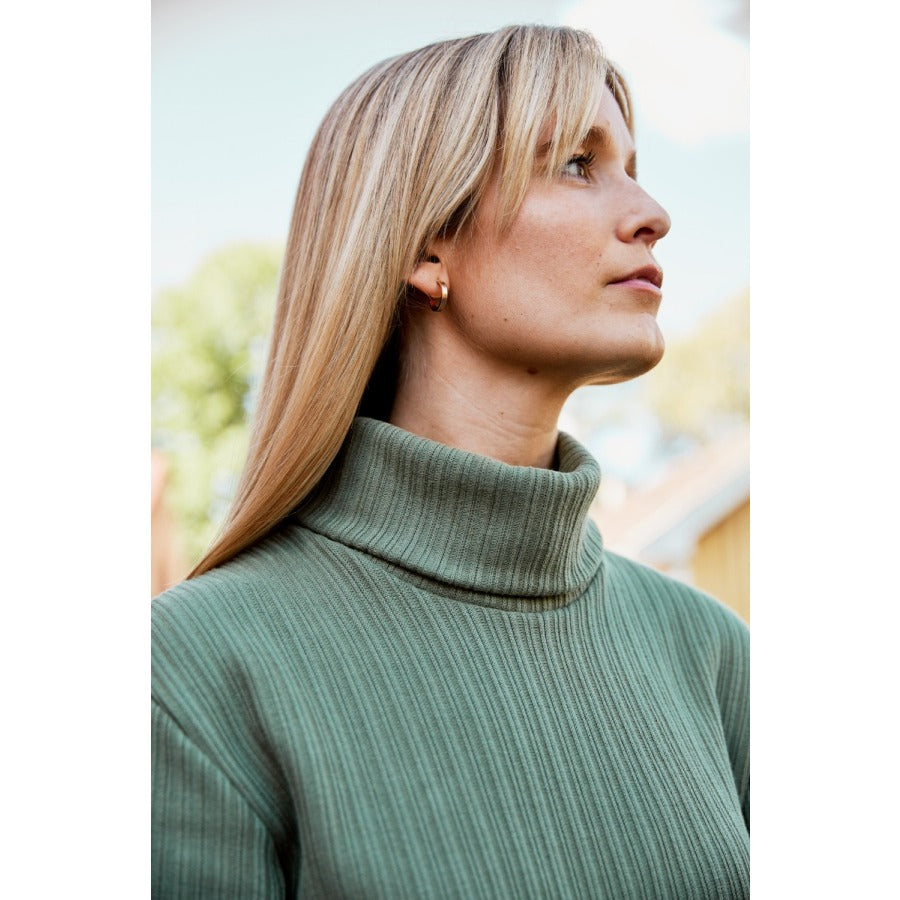 Close up of a white woman with long blonde hair wearing a green turtleneck sweater