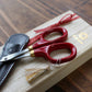Red lacquer handled embroidery scissors sitting on top of wooden presentation case