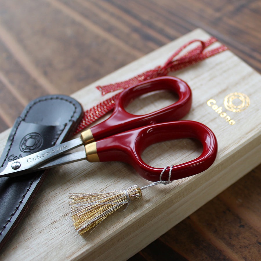 Red lacquer handled embroidery scissors sitting on top of wooden presentation case