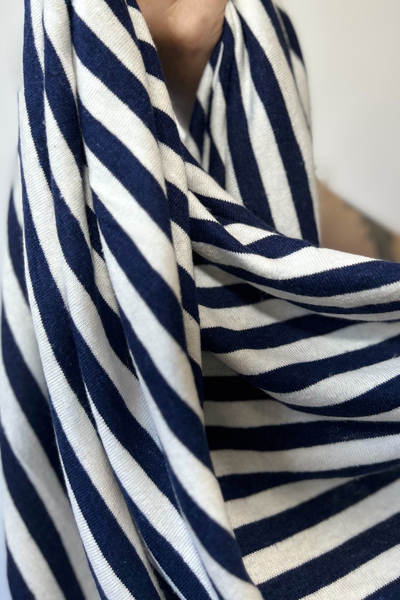 Close up of hand holding hemp and lyocell stripe jersey fabric in navy/white stripe