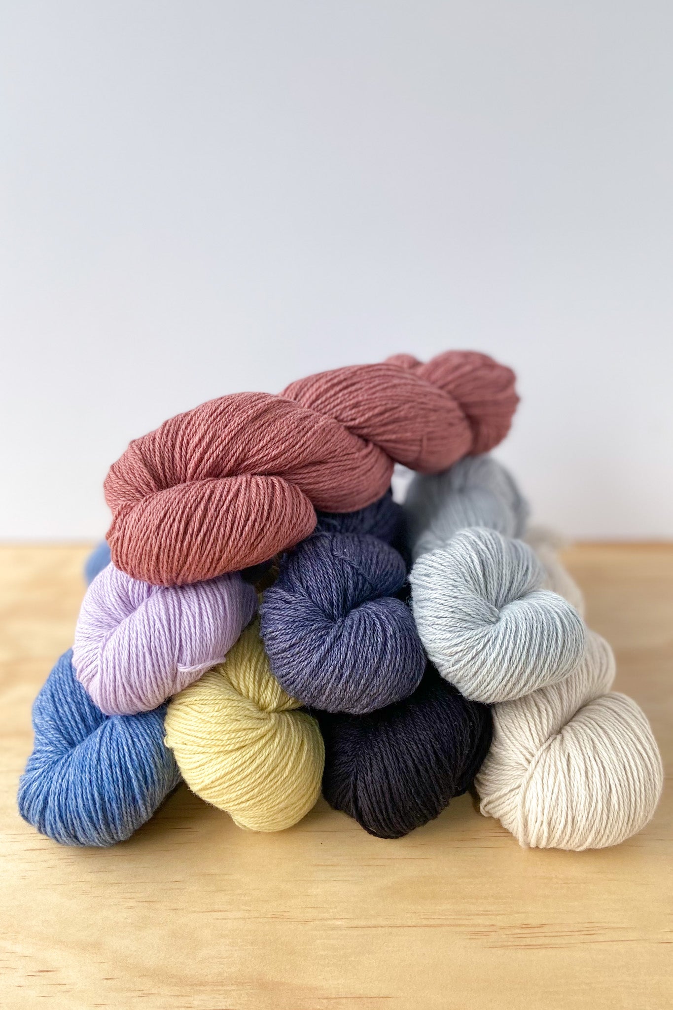 8 skeins of BC GARN Bio Balance 4ply organic cotton and organic wool knitting yarn in rust, violet, jeans, graphite, greenish yellow, black, silver and natural white.