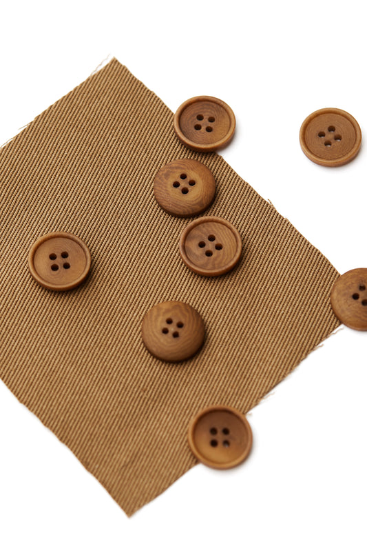 Pile of camel corozo sewing buttons scattered on top of matching fabric on white background