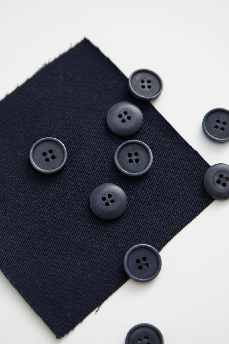 Navy corozo sewing buttons scattered on top of matching fabric swatch and white background