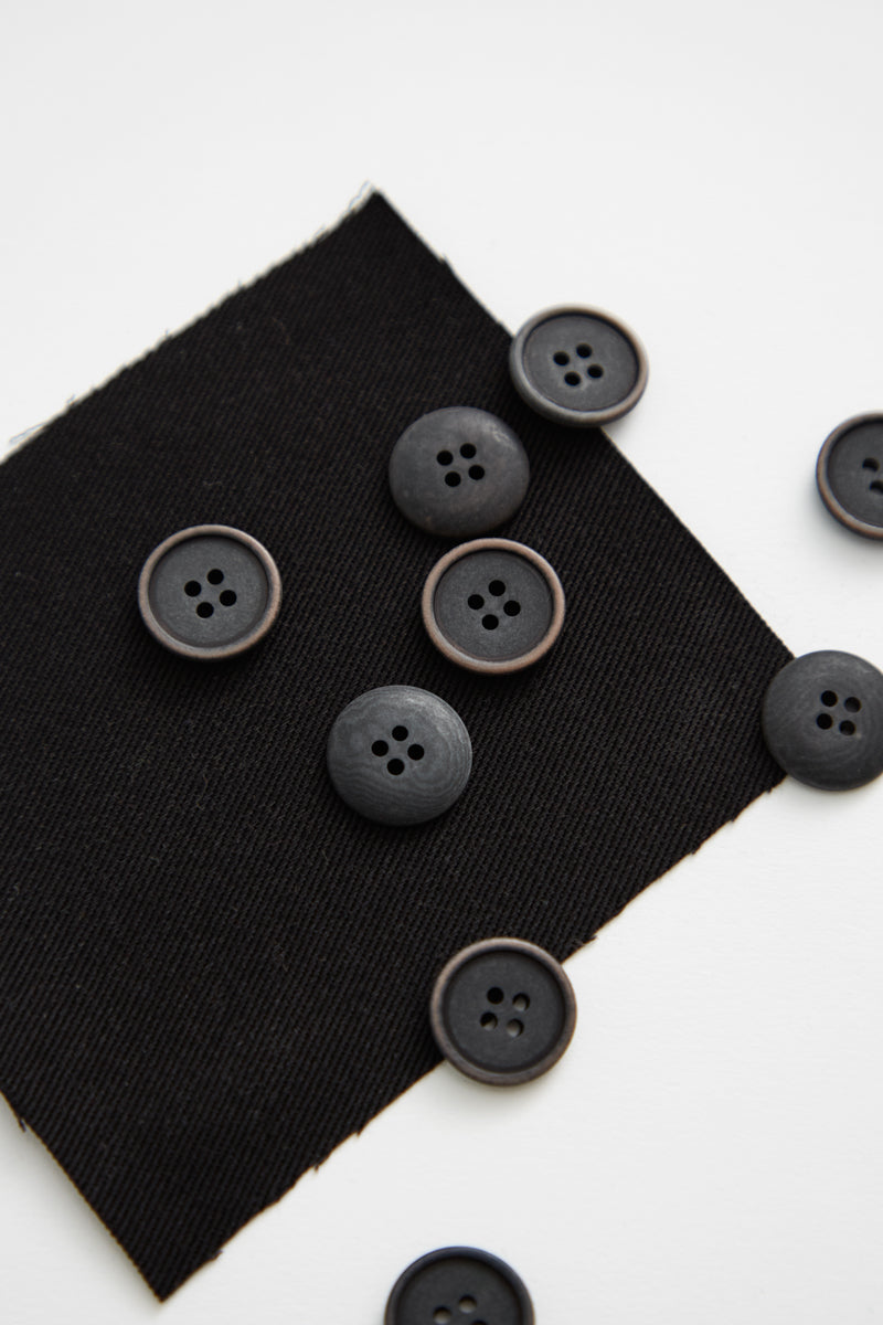 Collection of black corozo sewing buttons on piece of black fabric with white background