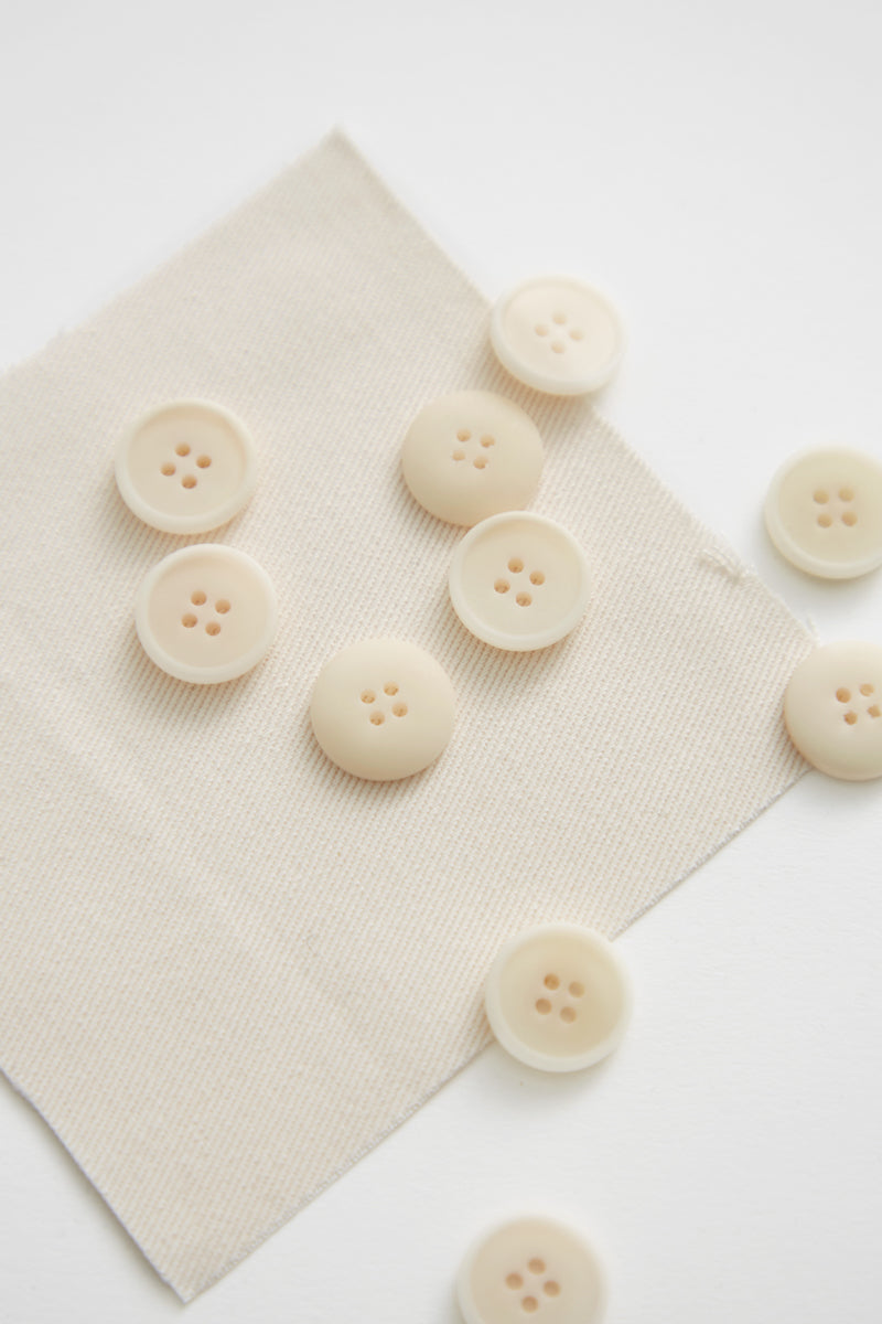 Creamy white corozo sewing buttons scattered on matching fabric swatch