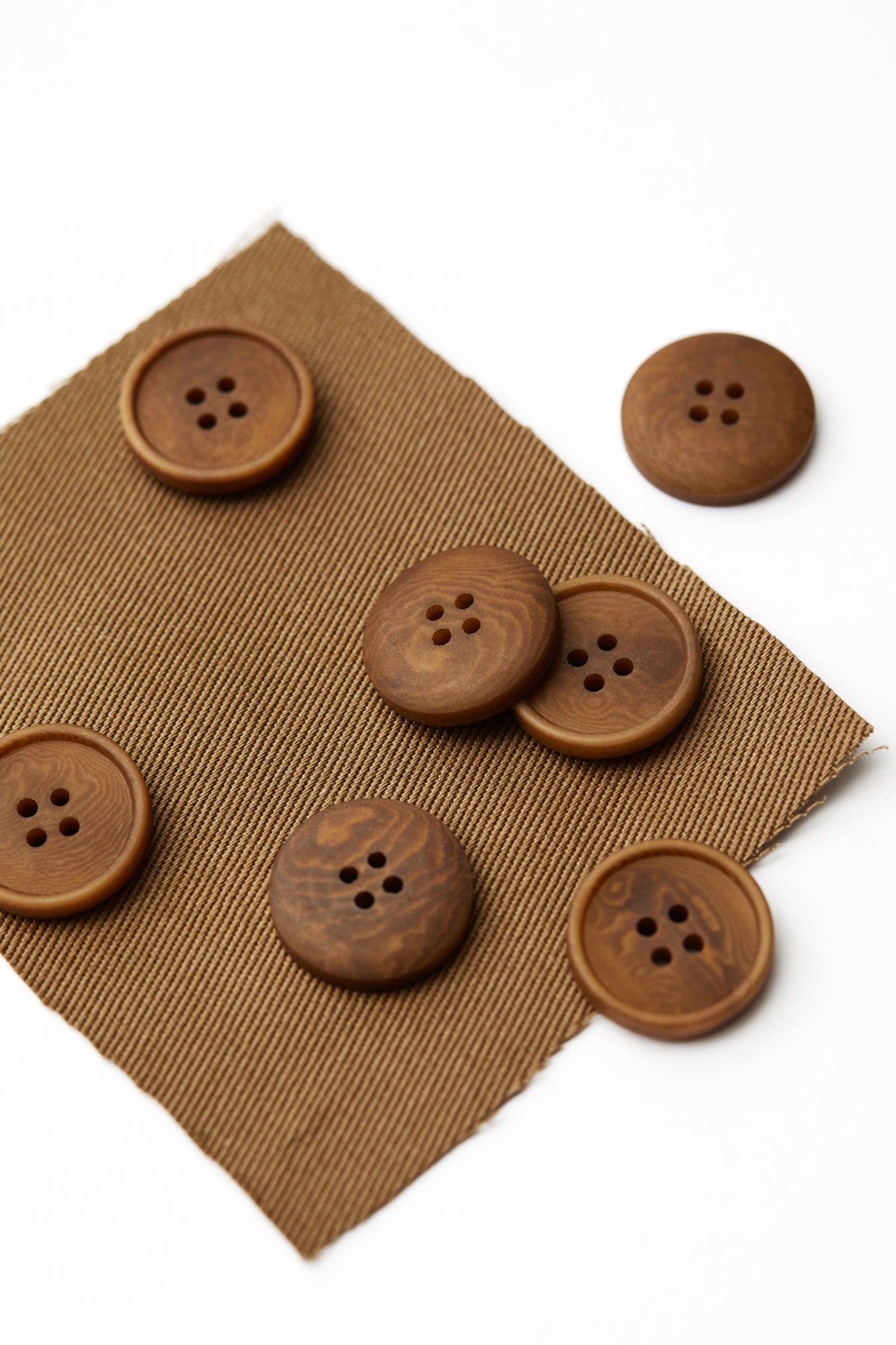 Close up of camel Corozo sewing buttons scattered on top of matching fabric swatch
