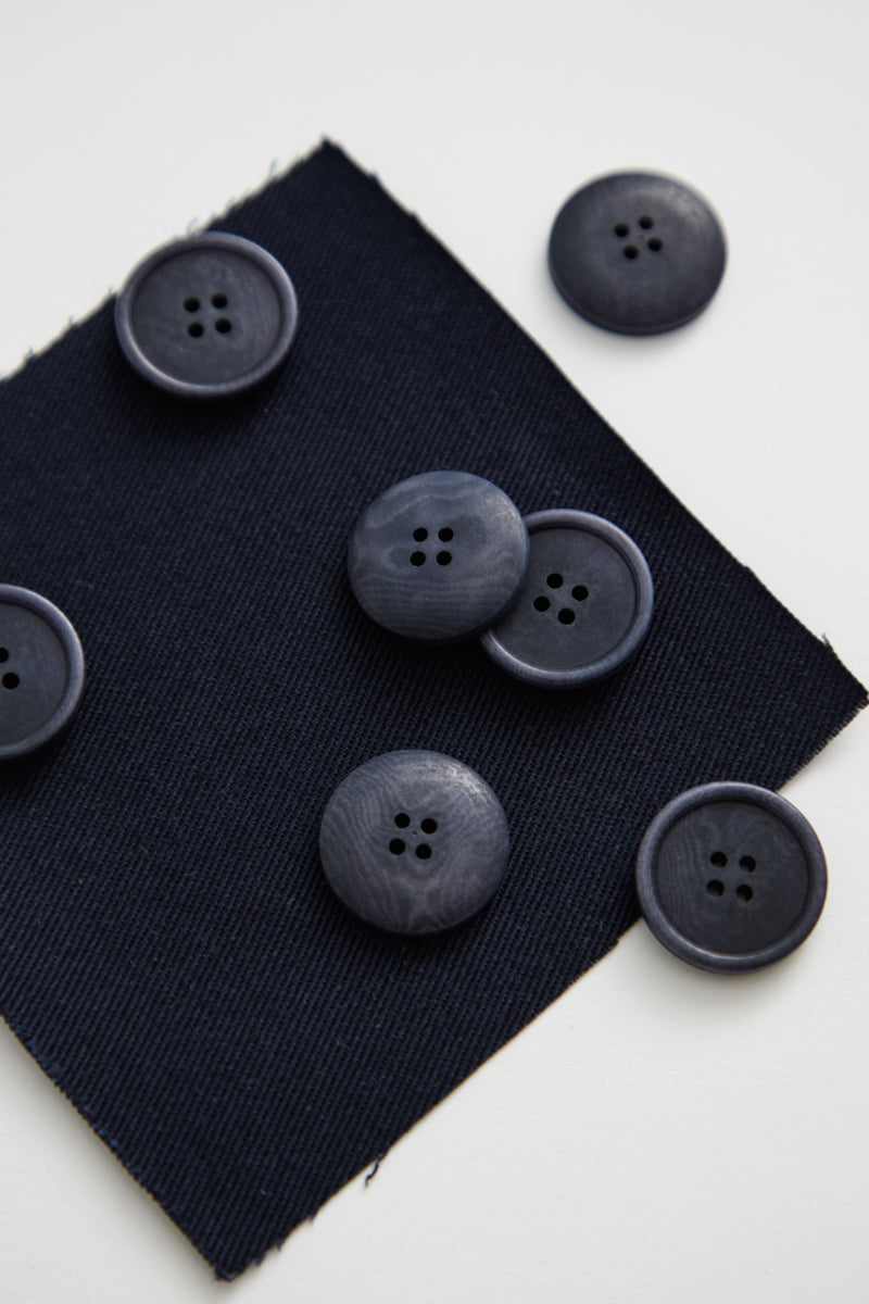 Close up of navy corozo buttons scattered on top of matching fabric swatch on white background