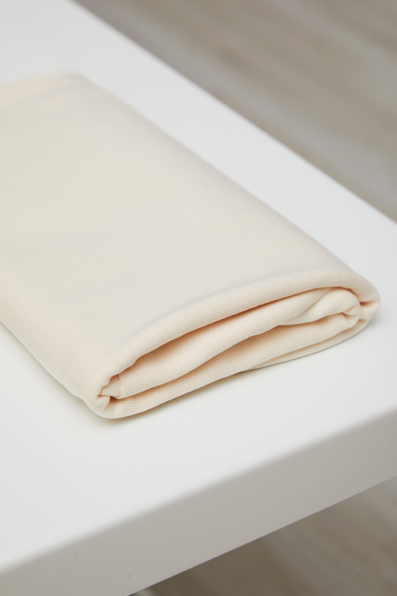 Cream coloured organic cotton and tencel jersey knit sewing fabric folded on top of white table