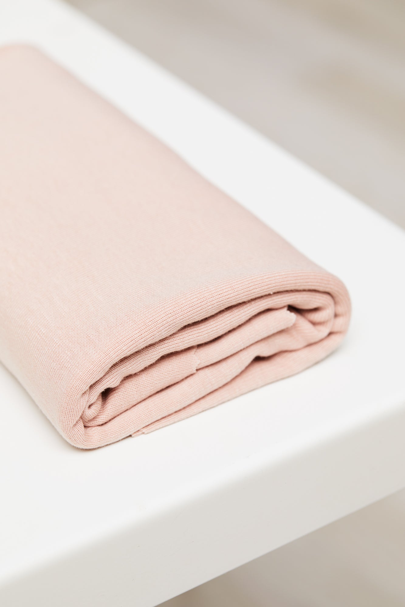Powder pink organic cotton and tencel knit jersey fabric folded on top of white table