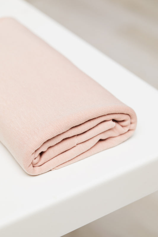 Powder pink organic cotton and tencel knit jersey fabric folded on top of white table