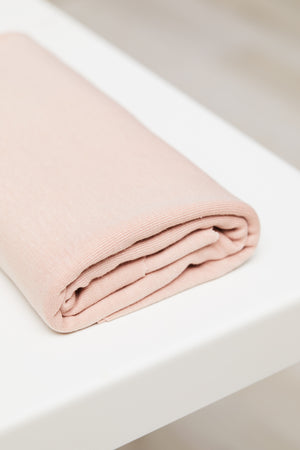Powder pink organic cotton and tencel knit jersey fabric folded on top of white table