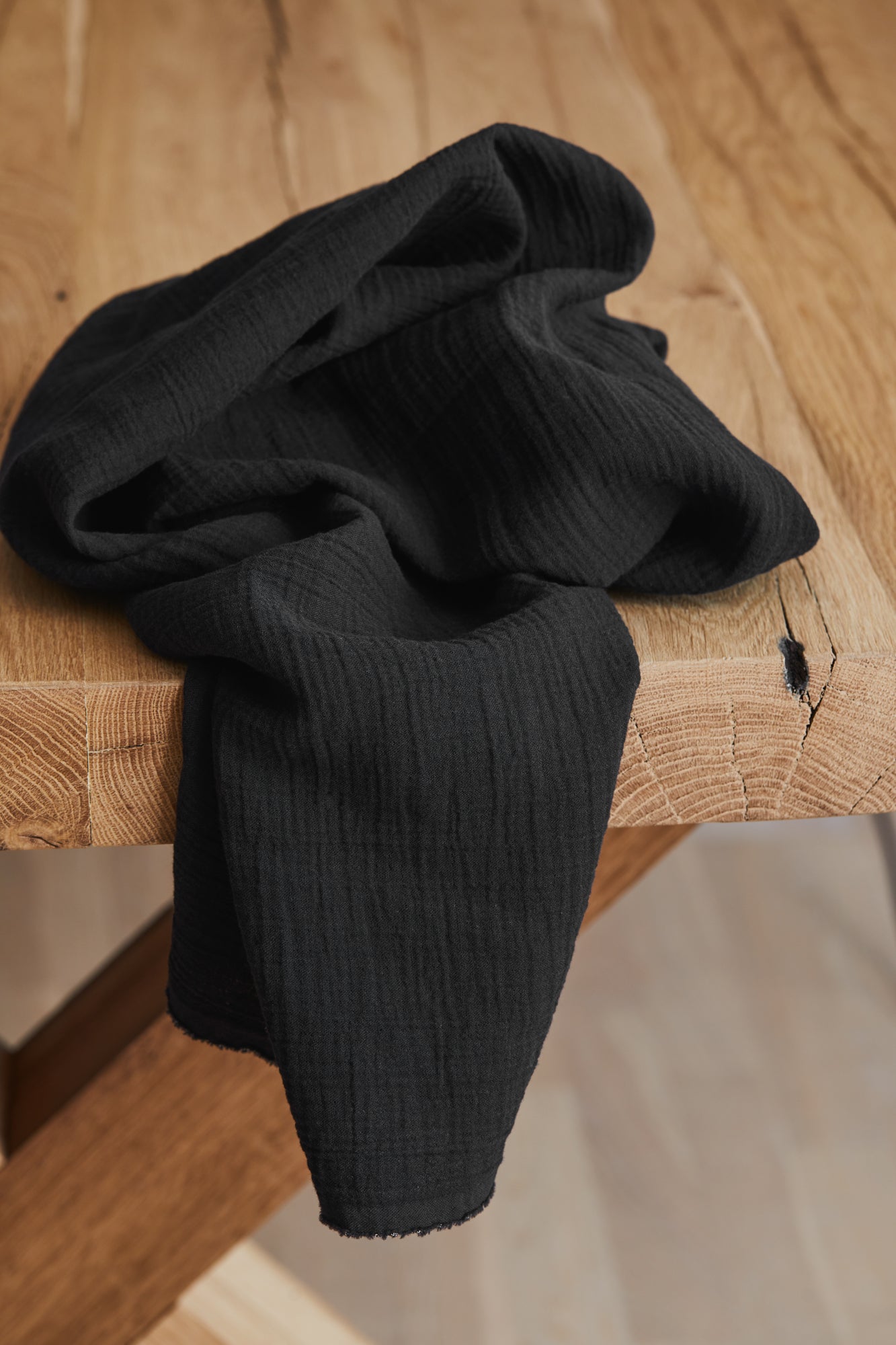Organic cotton double gauze crinkle sewing fabric in black, draped over wooden table
