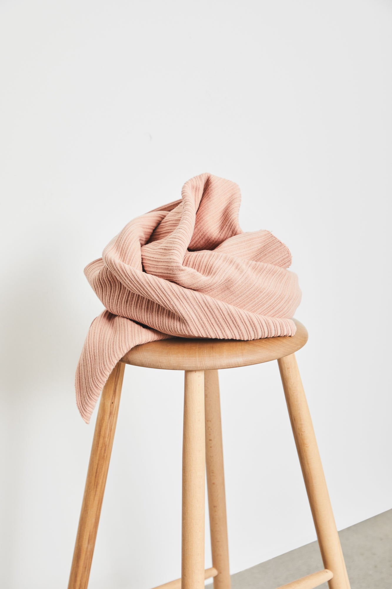 Chunky organic cotton ribbed knit fabric in colour rose (pale pink), piled on top of wooden stool