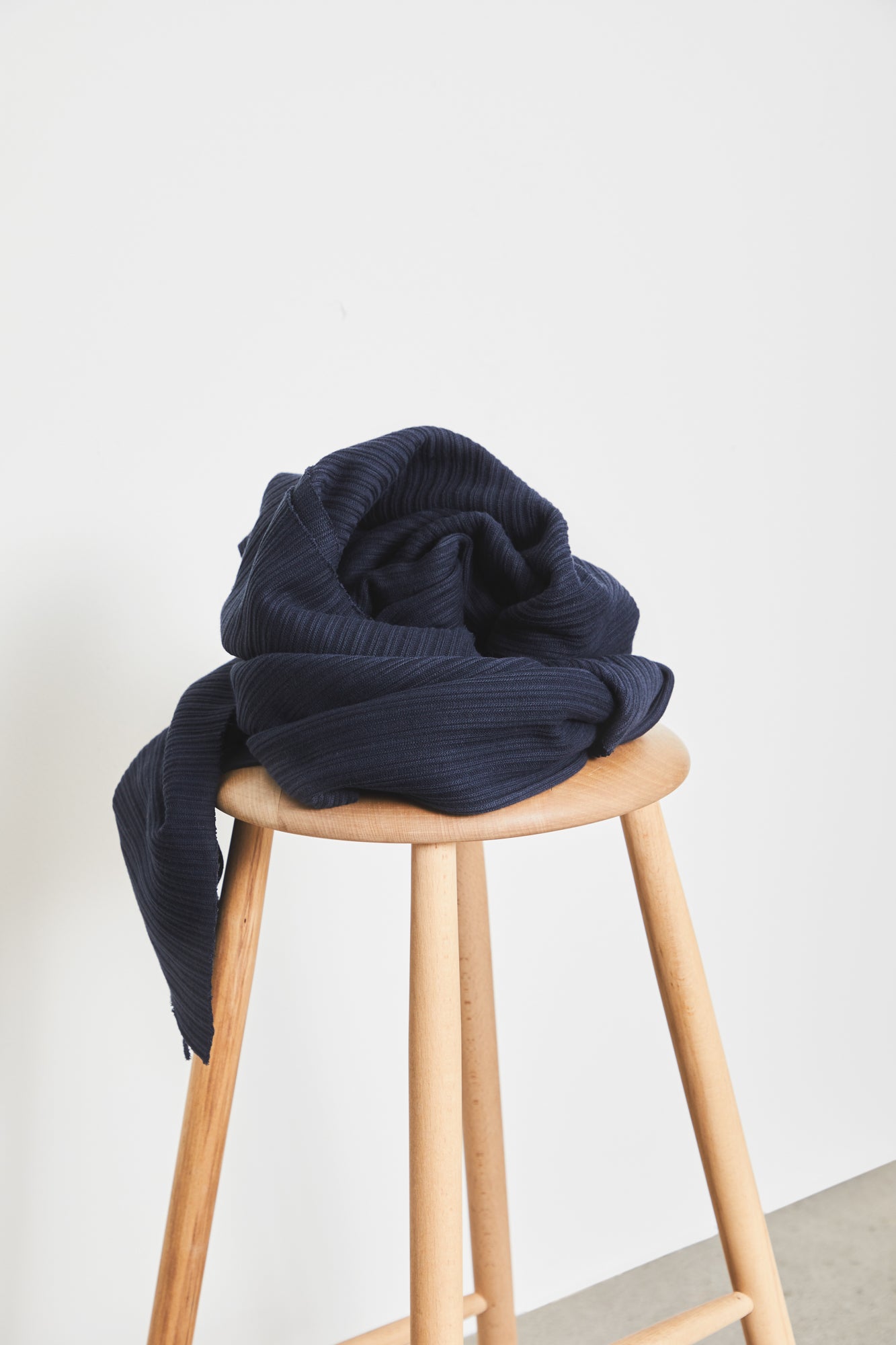Chunky organic cotton ribbed knit sewing fabric in colour navy, piled on top of wooden stool
