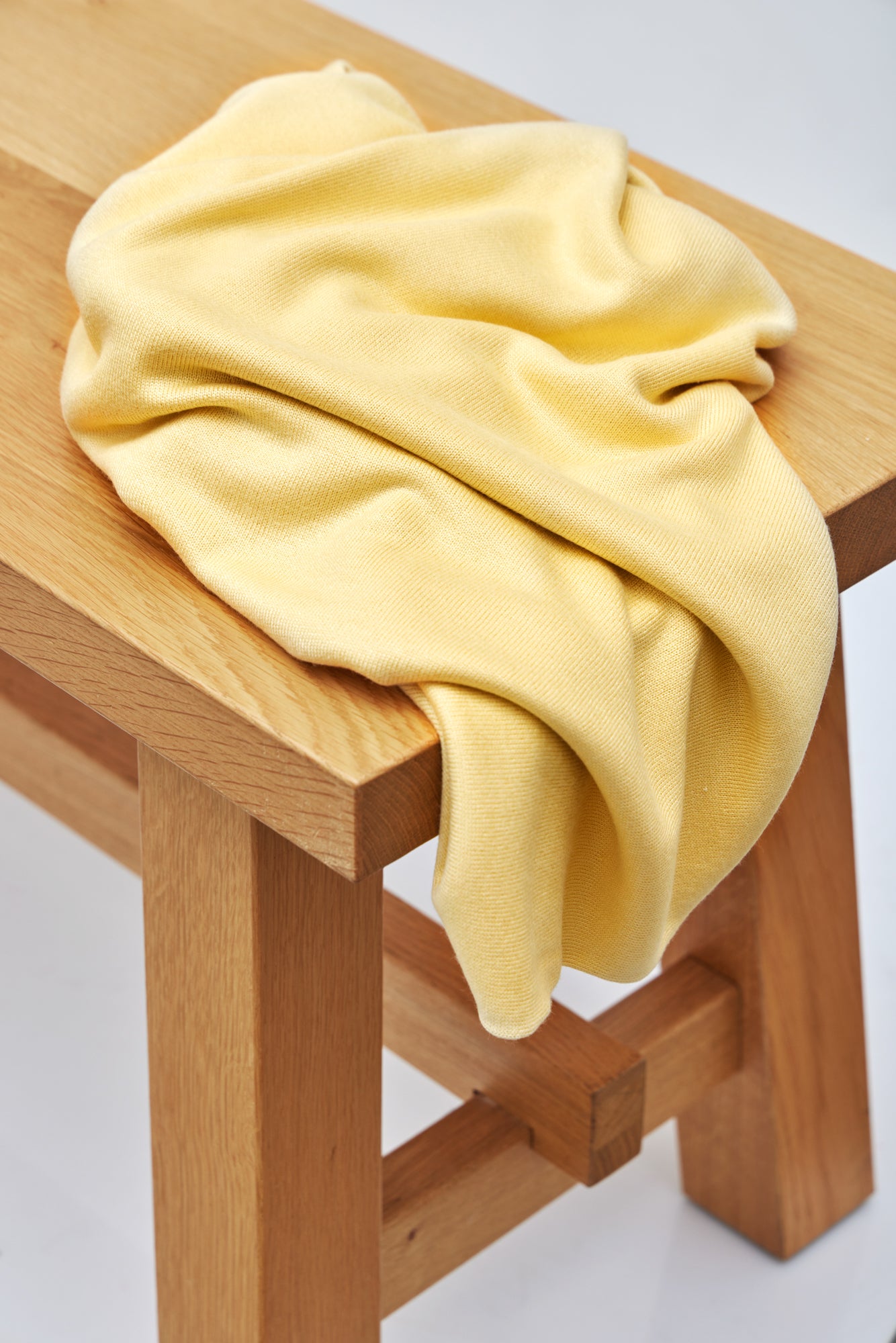 Yellow Ecovero knit sewing fabric draped over wooden bench