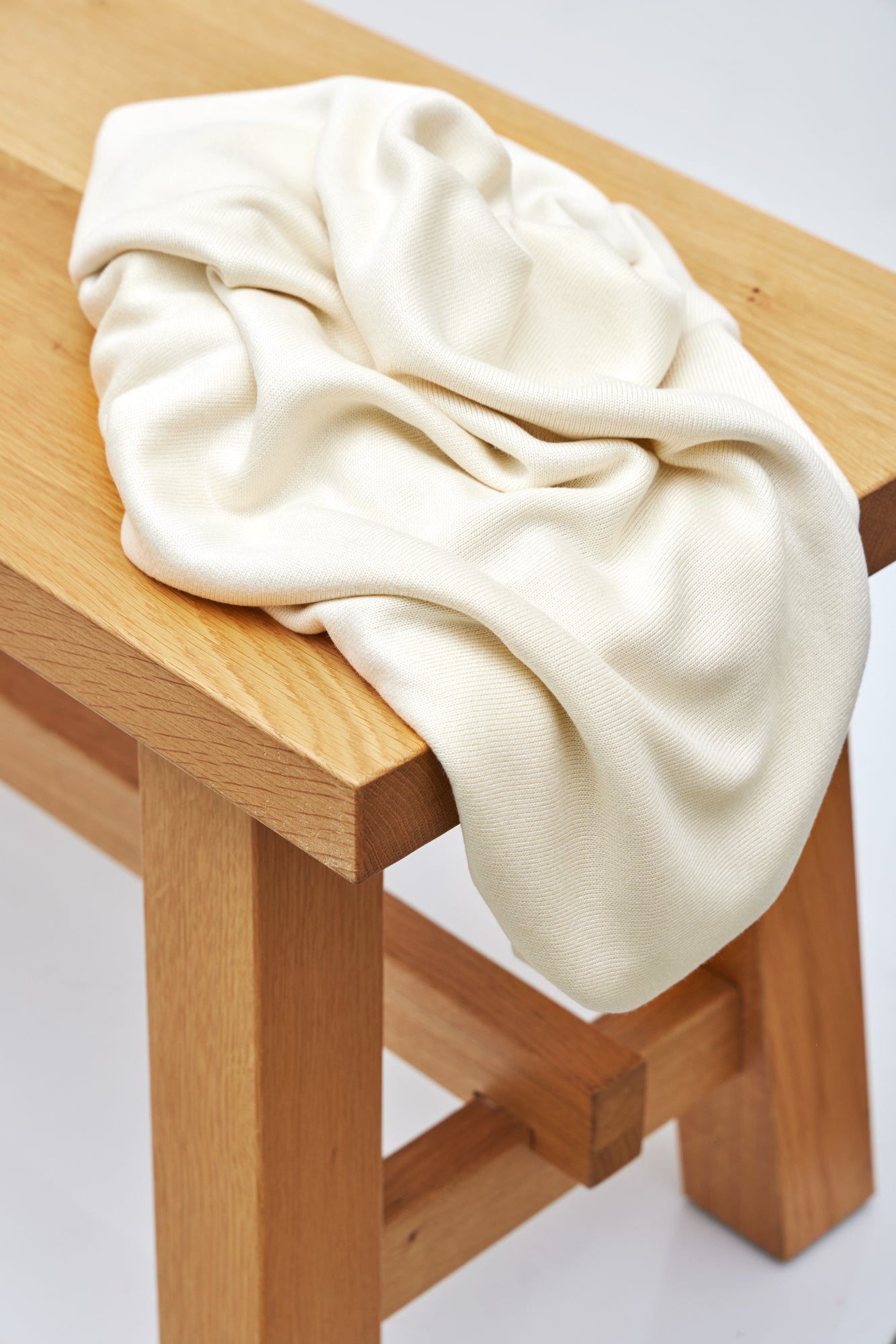 Shell (cream) Ecovero knit sewing fabric draped over wooden bench