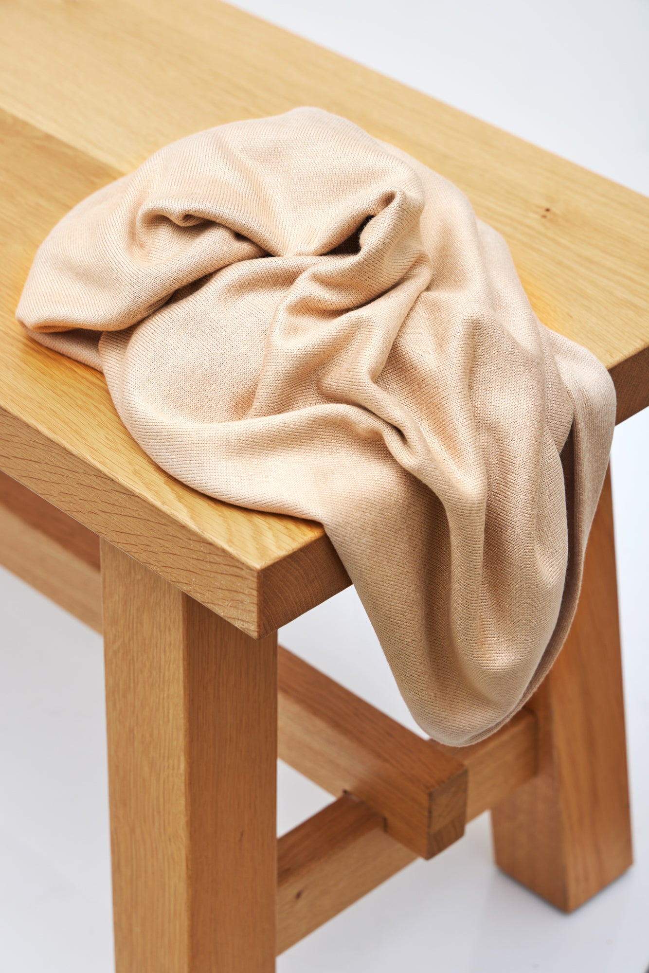 Warm sand (beige) Ecovero knit sewing fabric draped over wooden bench