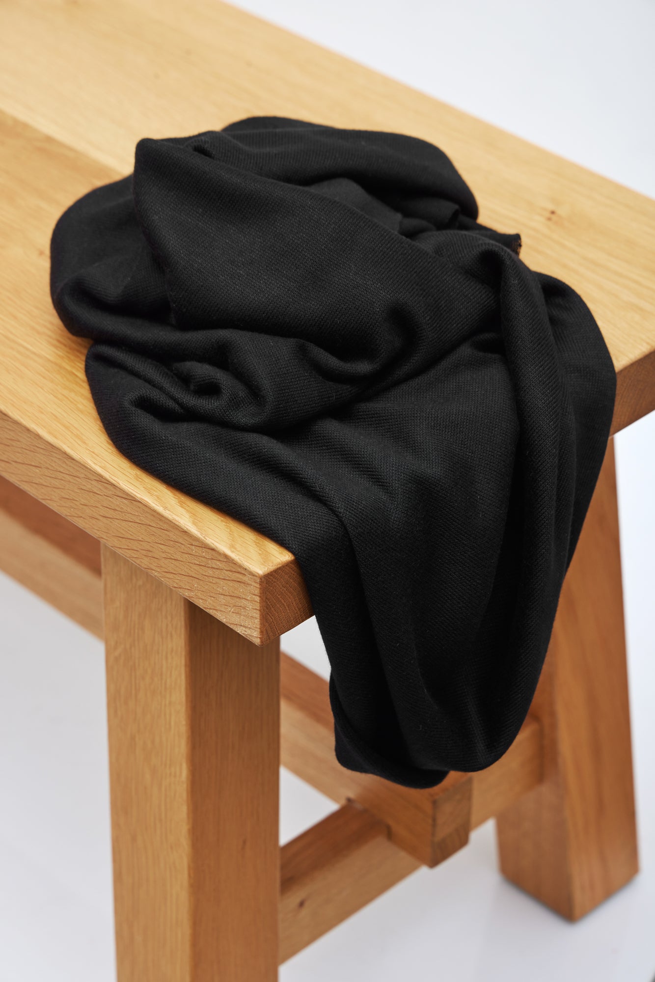 Black Ecovero knit sewing fabric draped over wooden bench
