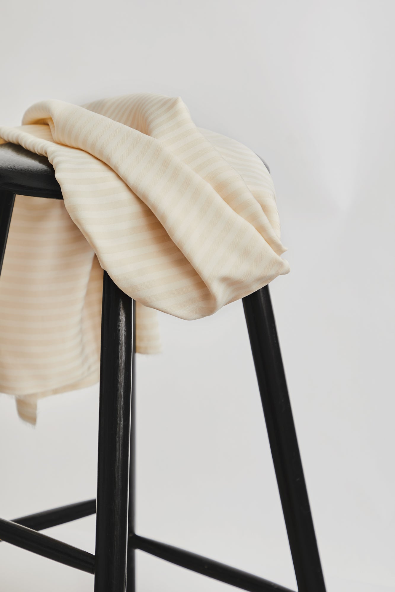 Two Tone stripe twill tencel, sustainable woven fabric in shell colour draped on black stool